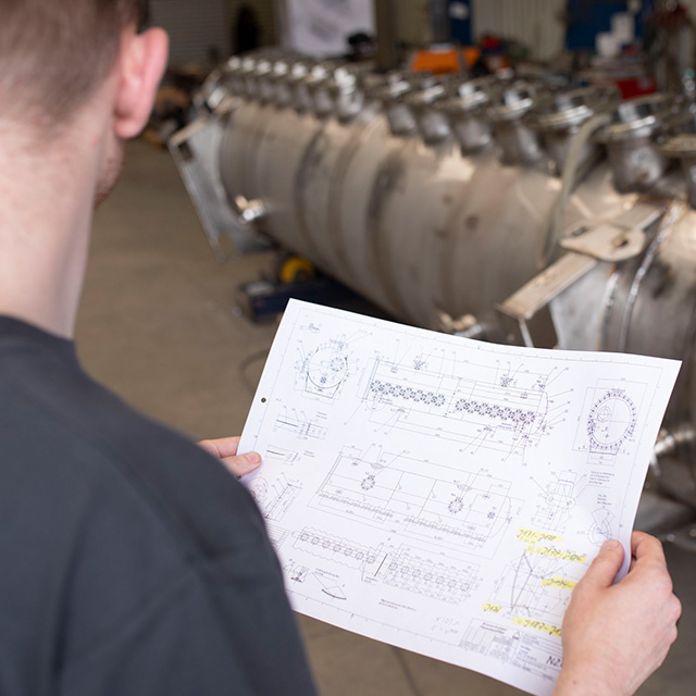 Techniker prüft Konstruktionszeichnung vor industrieller Anlage - Hatec Industriemontagen