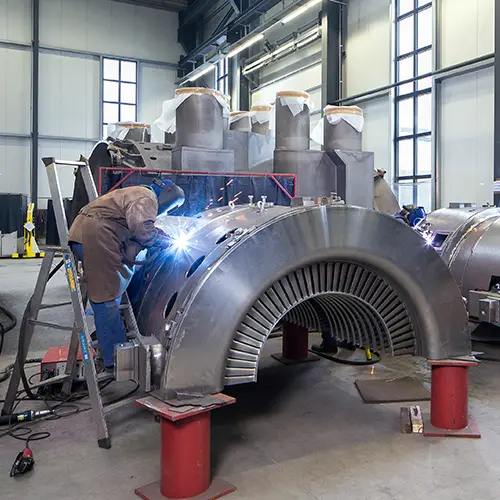 Fachkr&auml;fte f&uuml;hren pr&auml;zise Schwei&szlig;arbeiten an einem gro&szlig;en Turbinengeh&auml;use in der Hatec Industriemontagehalle aus mit sichtbaren Anpassungen und Reparaturen am Metallbauteil